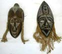 The left one: black oval shape lady head with eye-closed design wooden mask with rope earring.  The right one: black olive shape head wooden mask with empty eye hole and triangular mouth-open 
